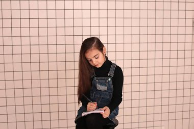 Sekiz yaşında, uzun saçlı, siyah balıkçı yakalı ve kotlu bir elbise giyen gülümseyen genç bir kız.