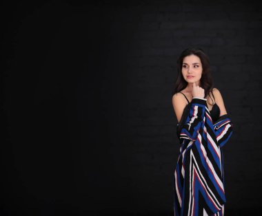 Siyah elbiseli, siyah saçlı ve çizgili hırkalı güzel bir kadının portresi. Çizmelerinin üzerinde koyu bir arka plan var.