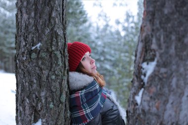 Beautiful girl with green eyes and ginger hair in a red hat on a walk in a winter snowy forest