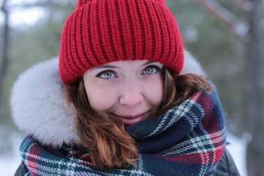 Beautiful girl with green eyes and ginger hair in a red hat on a walk in a winter snowy forest