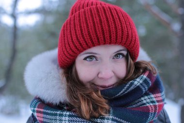 Beautiful girl with green eyes and ginger hair in a red hat on a walk in a winter snowy forest