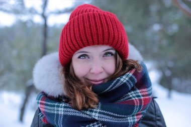 Beautiful girl with green eyes and ginger hair in a red hat on a walk in a winter snowy forest