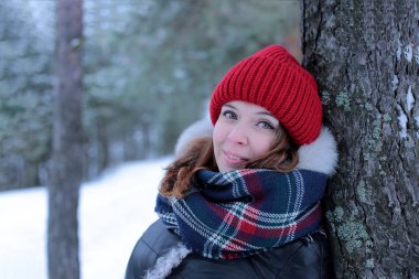 Beautiful girl with green eyes and ginger hair in a red hat on a walk in a winter snowy forest