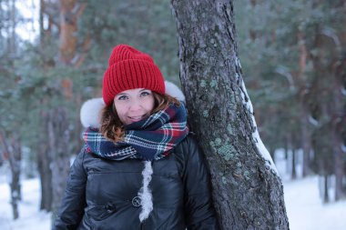 Beautiful girl with green eyes and ginger hair in a red hat on a walk in a winter snowy forest