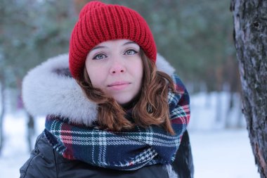 Beautiful girl with green eyes and ginger hair in a red hat on a walk in a winter snowy forest