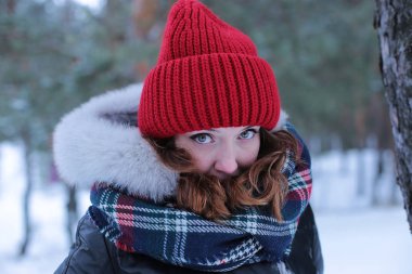 Beautiful girl with green eyes and ginger hair in a red hat on a walk in a winter snowy forest