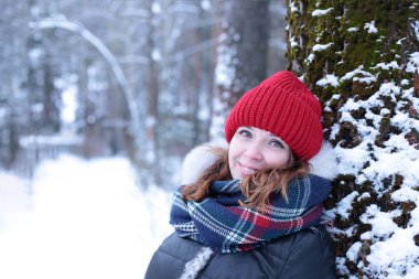 Beautiful girl with green eyes and ginger hair in a red hat on a walk in a winter snowy forest