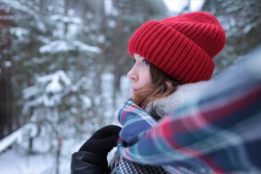 Beautiful girl with green eyes and ginger hair in a red hat on a walk in a winter snowy forest