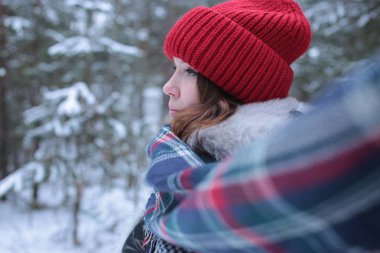 Beautiful girl with green eyes and ginger hair in a red hat on a walk in a winter snowy forest