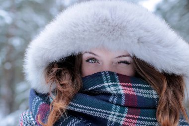 Beautiful girl with green eyes and ginger hair in a red hat on a walk in a winter snowy forest