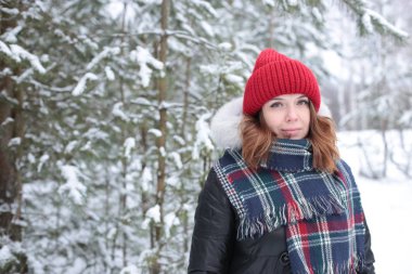 Beautiful girl with green eyes and ginger hair in a red hat on a walk in a winter snowy forest