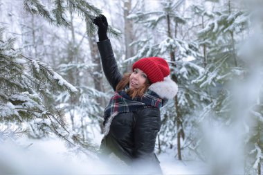 Beautiful girl with green eyes and ginger hair in a red hat on a walk in a winter snowy forest