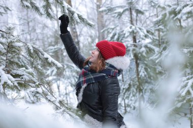 Beautiful girl with green eyes and ginger hair in a red hat on a walk in a winter snowy forest