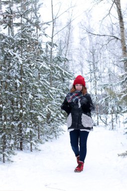 Beautiful girl with green eyes and ginger hair in a red hat on a walk in a winter snowy forest
