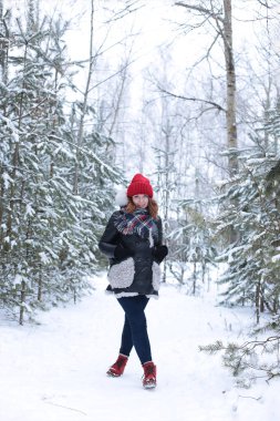 Beautiful girl with green eyes and ginger hair in a red hat on a walk in a winter snowy forest