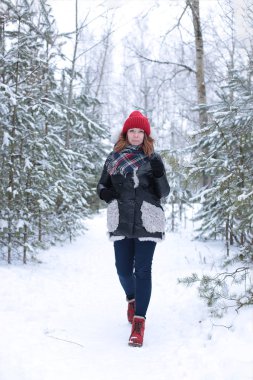 Beautiful girl with green eyes and ginger hair in a red hat on a walk in a winter snowy forest