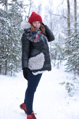 Beautiful girl with green eyes and ginger hair in a red hat on a walk in a winter snowy forest