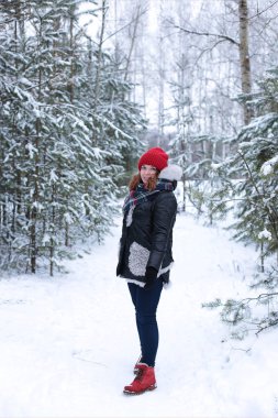 Beautiful girl with green eyes and ginger hair in a red hat on a walk in a winter snowy forest