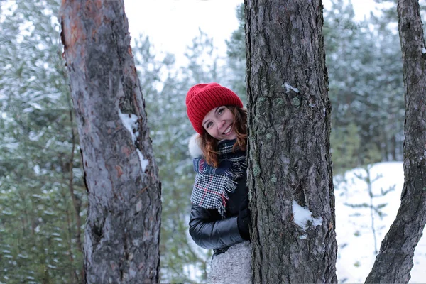 冬の雪の森を歩いていると 赤い帽子の中に緑の目と生姜の髪の美しい女の子 — ストック写真
