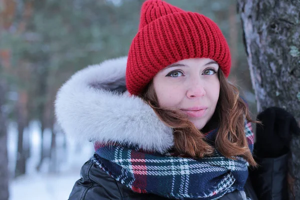 Beautiful girl with green eyes and ginger hair in a red hat on a walk in a winter snowy forest