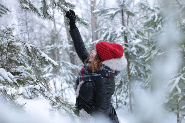 Beautiful girl with green eyes and ginger hair in a red hat on a walk in a winter snowy forest