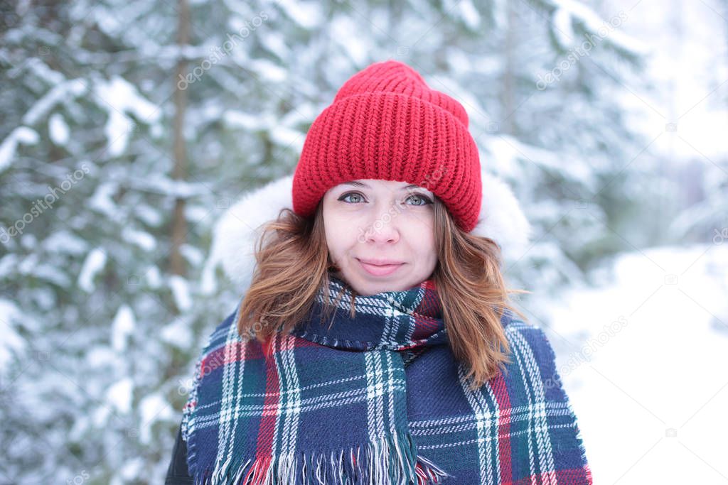 Beautiful girl with green eyes and ginger hair in a red hat on a walk in a winter snowy forest