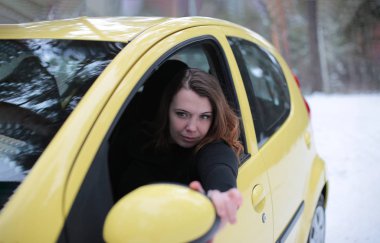 Beautiful young woman with green eyes and red hair in a yellow car in a winter snowy forest