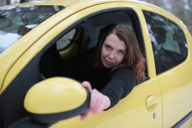 Beautiful young woman with green eyes and red hair in a yellow car in a winter snowy forest