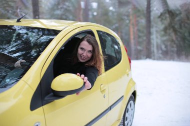 Beautiful young woman with green eyes and red hair in a yellow car in a winter snowy forest