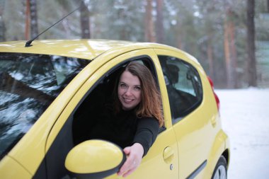 Beautiful young woman with green eyes and red hair in a yellow car in a winter snowy forest