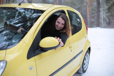 Beautiful young woman with green eyes and red hair in a yellow car in a winter snowy forest