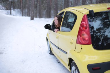 Beautiful young woman with green eyes and red hair in a yellow car in a winter snowy forest