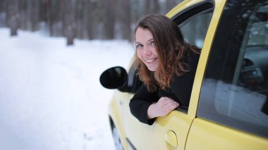 Beautiful young woman with green eyes and red hair in a yellow car in a winter snowy forest