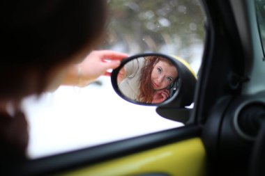 Beautiful young woman with green eyes and red hair in a yellow car in a winter snowy forest