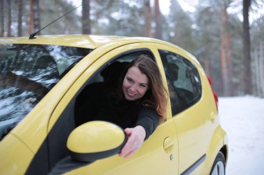 Beautiful young woman with green eyes and red hair in a yellow car in a winter snowy forest