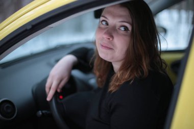 Beautiful young woman with green eyes and red hair in a yellow car in a winter snowy forest clipart