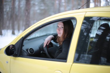 Beautiful young woman with green eyes and red hair in a yellow car in a winter snowy forest