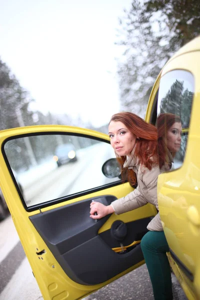 冬の雪の森の中の黄色の車の中で緑の目と赤い髪の美しい若い女性 — ストック写真