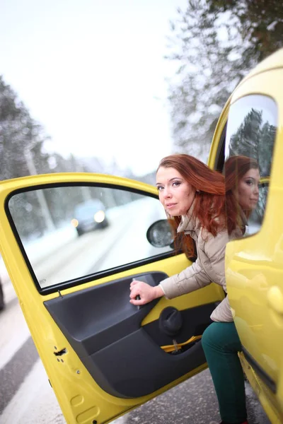 美丽的年轻女子 绿色的眼睛 红色的头发 开着一辆黄色的车 在冬季的雪地里 — 图库照片