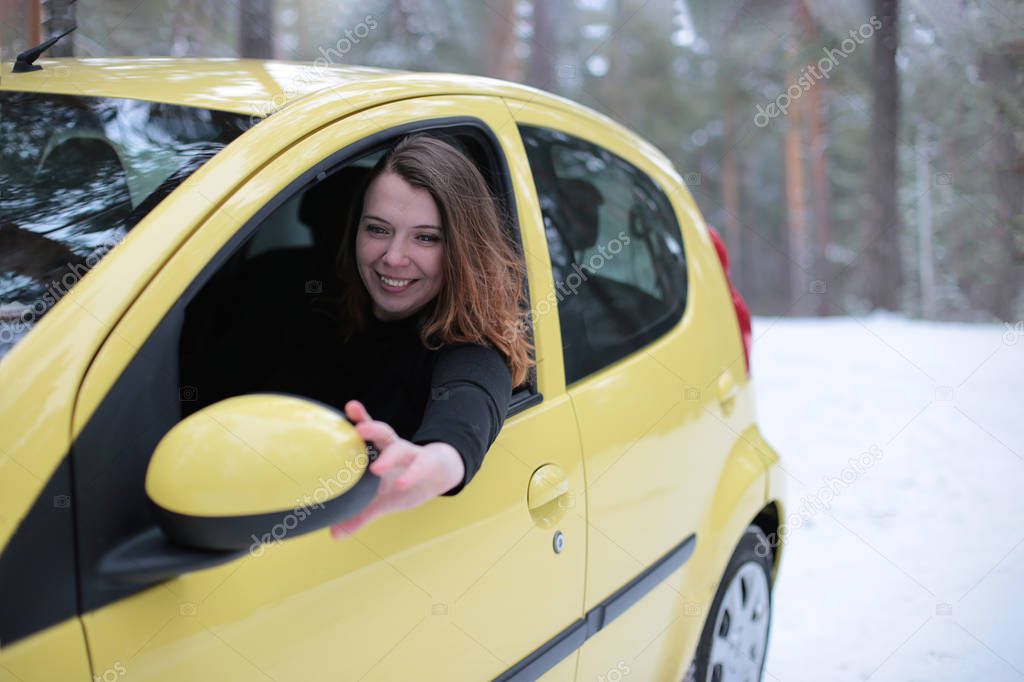 Beautiful young woman with green eyes and red hair in a yellow car in a winter snowy forest