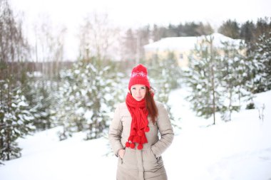 Güzel, çekici, gülümseyen, yeşil gözlü, kızıl saçlı genç bir kadın kışın karlı bir ormanda keyifli bir şekilde yürüyor.