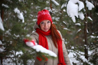 Güzel, çekici, gülümseyen, yeşil gözlü, kızıl saçlı genç bir kadın kışın karlı bir ormanda keyifli bir şekilde yürüyor.