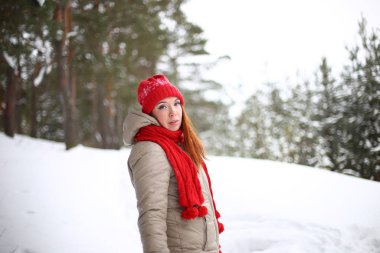 Güzel, çekici, gülümseyen, yeşil gözlü, kızıl saçlı genç bir kadın kışın karlı bir ormanda keyifli bir şekilde yürüyor.