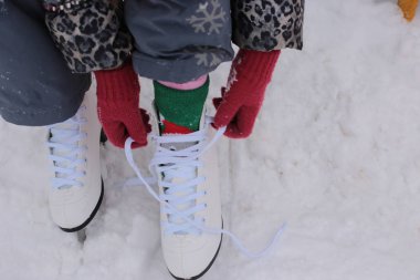 woman legs wearing white leather skates, training on a frosen snowy skating rink in winter