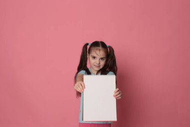 funny girl of eight years old and a colored sheet of paper free space for writing on a pale pink background