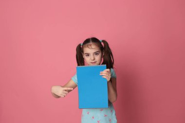 funny girl of eight years old and a colored sheet of paper free space for writing on a pale pink background