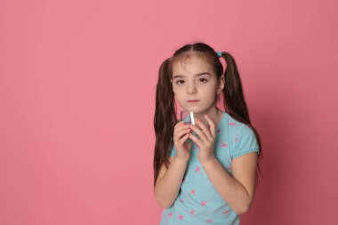 A beautiful girl of eight years drinks water from a transparent glass on a pink background in a blue T-shirt