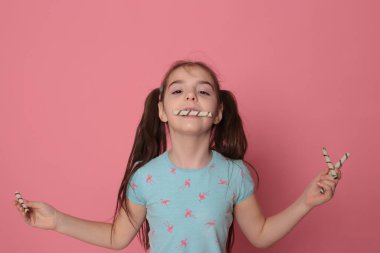 loving happy smiling girl with two ponytail long hair in a good fun mood eating sweet treats on a bright pink background