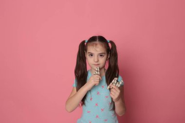 loving happy smiling girl with two ponytail long hair in a good fun mood eating sweet treats on a bright pink background