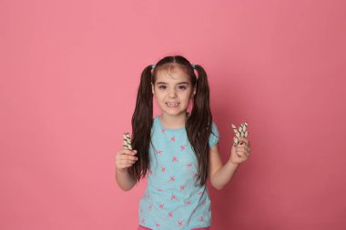 loving happy smiling girl with two ponytail long hair in a good fun mood eating sweet treats on a bright pink background
